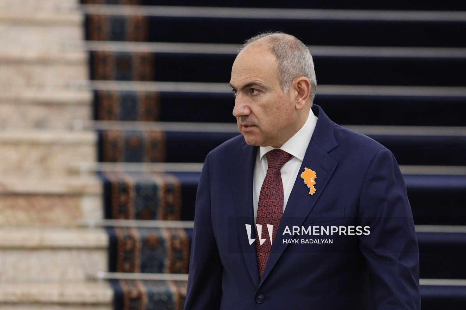 Представитель правительства Армении с нагрудным значком в форме карты страны у здания парламента