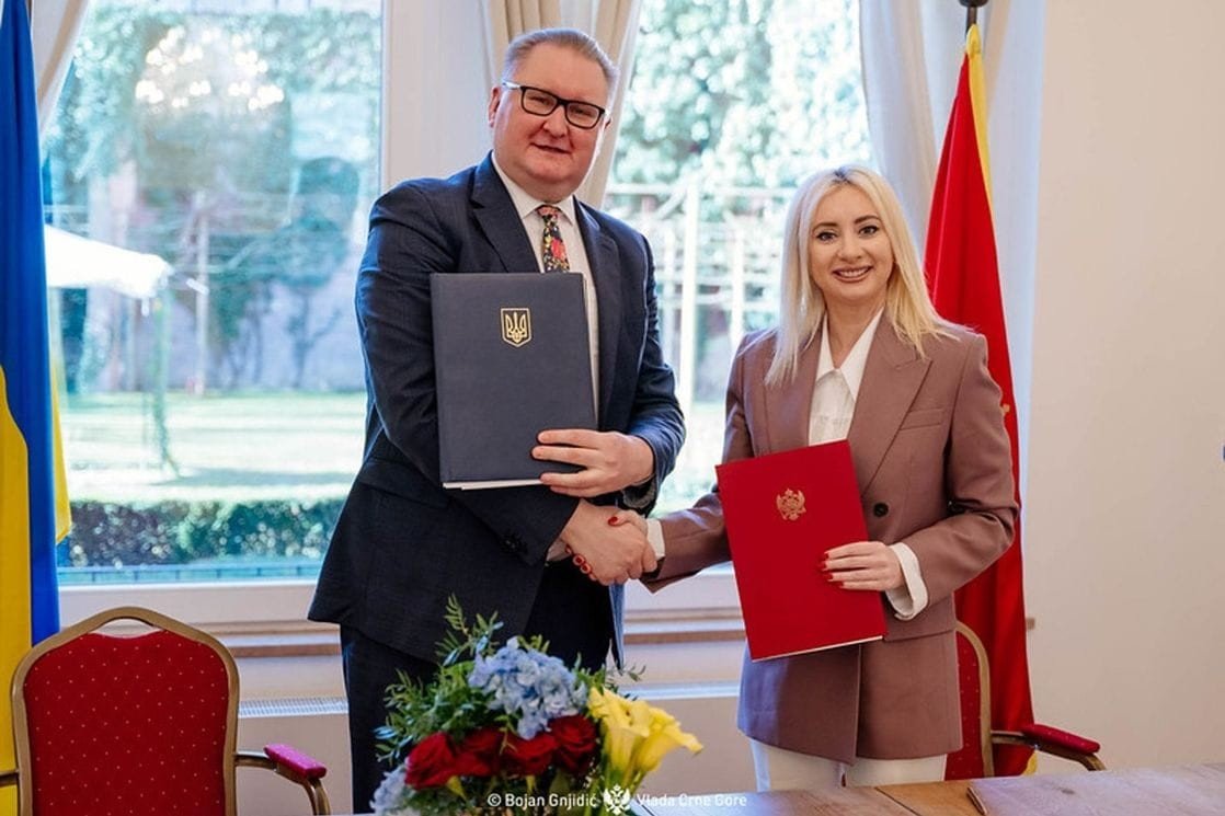 Тарас Качка и Маида Горчевич обмениваются рукопожатием после подписания Меморандума, держа папки с подписанными документами на фоне флагов Украины и Черногории