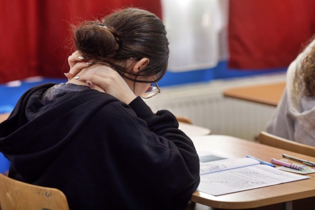 Симуляция BAC в Румынии: худшие работы за десятилетия Ученица сидит за партой, опустив голову и держась за шею от напряжения, во время письменного экзамена в учебном классе