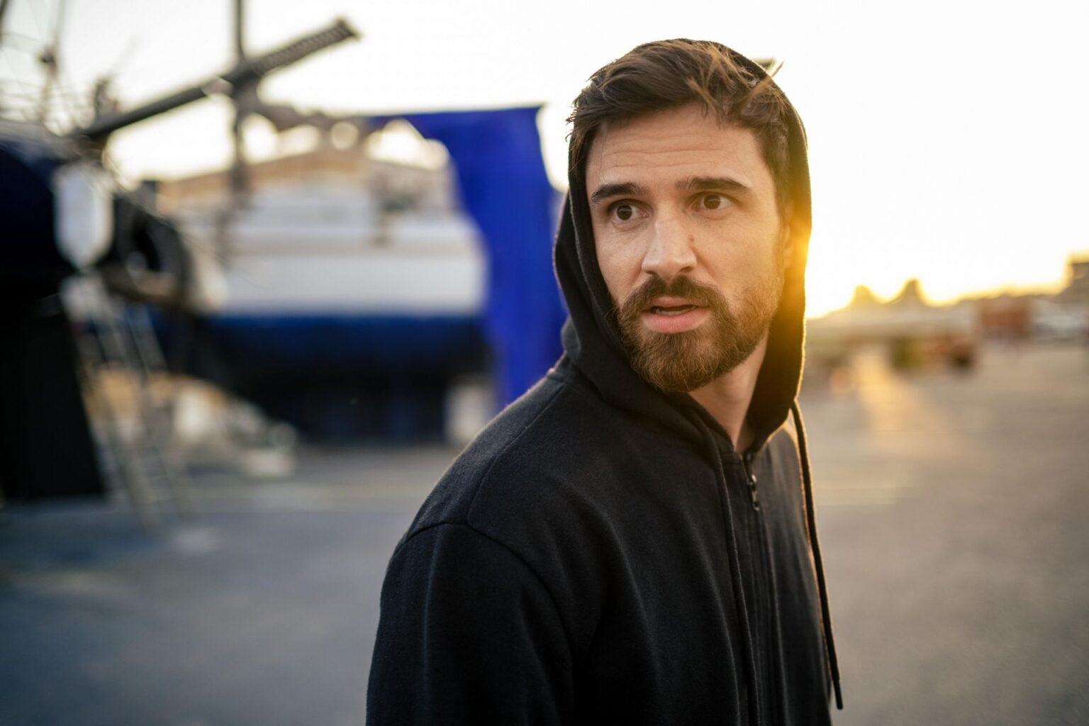 Румынский «Джеймс Бонд» расколол публику на премьере Актёр в капюшоне на фоне порта на закате — кадр из фильма «Тот март»