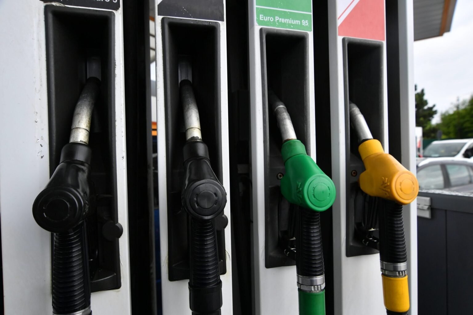 Крупный план топливных пистолетов на автозаправочной станции — чёрные, зелёный и жёлтый рукоятки в гнёздах колонки