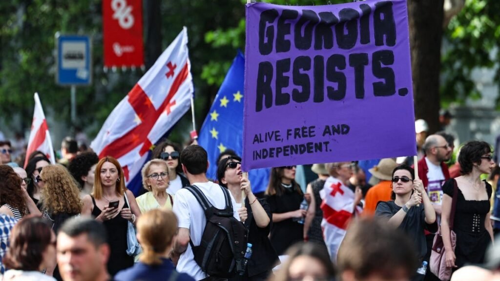 Массовый протест в Грузии с плакатом Georgia Resists и национальными флагами