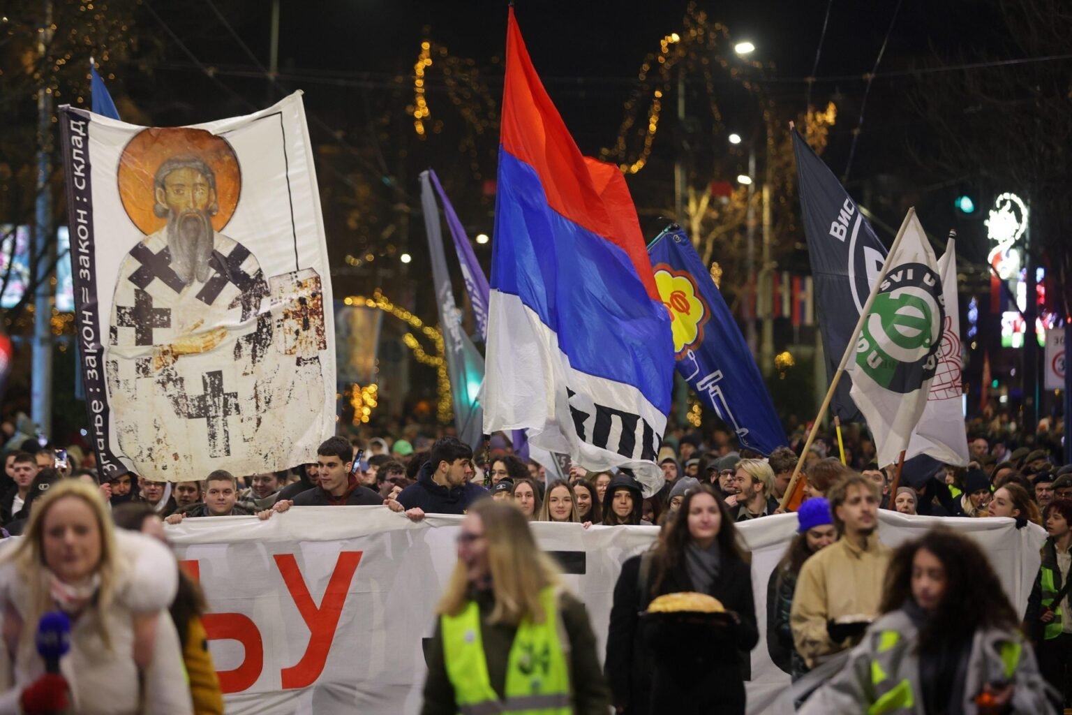 Ночное шествие протестующих в Белграде с сербскими флагами, транспарантами и студентами на фоне праздничных огней города. Фото: EUAlive