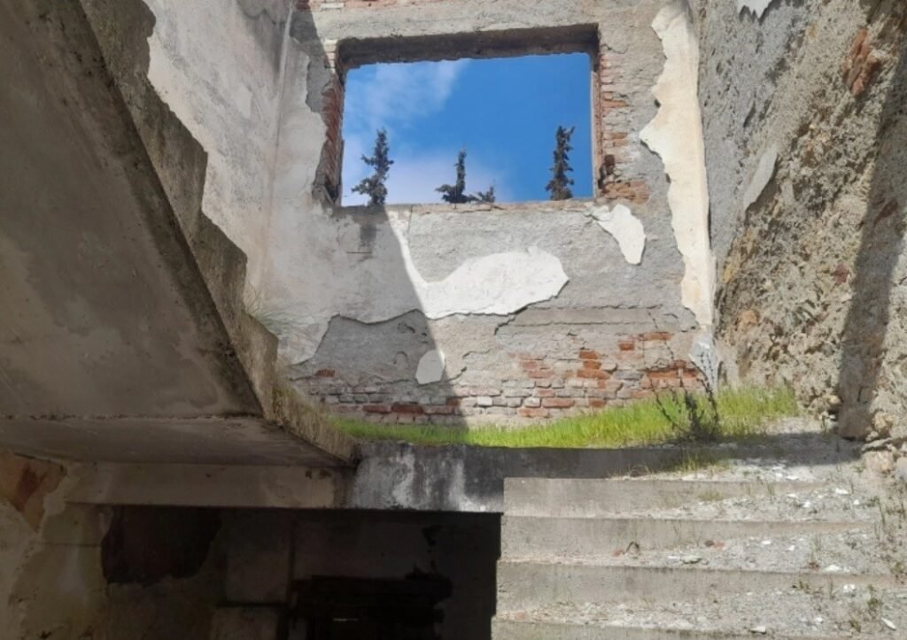 Школа с фреской у озера Дойран: руины ждут возрождения Руины старого школьного здания в Нов-Дойране: осыпавшаяся штукатурка обнажает кирпичную кладку на стенах лестничного пролёта, а оконный проём открывает вид на голубое небо и кипарисы