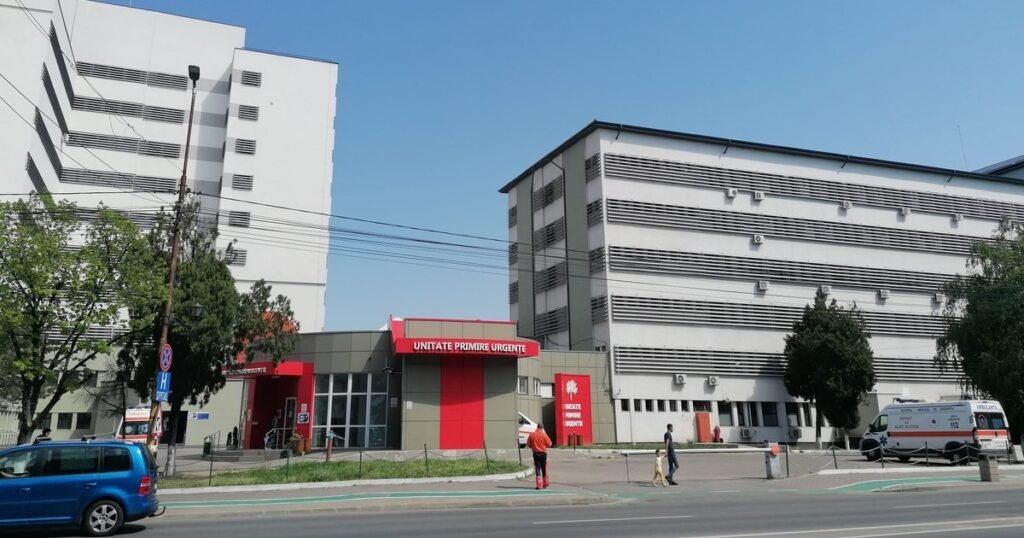 Здание Окружной больницы скорой помощи Слатина с красной вывеской приёмного отделения, справа видны машины скорой помощи