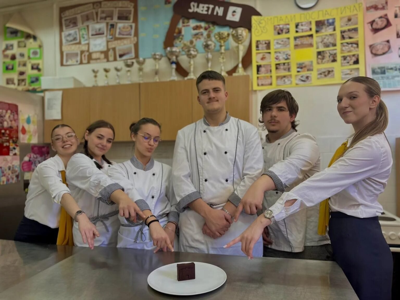 Шестеро учеников Угостительско-туристической школы Ниша позируют в поварской форме на школьной кухне, представляя тарелку с безглютеновым шоколадом из шпината
