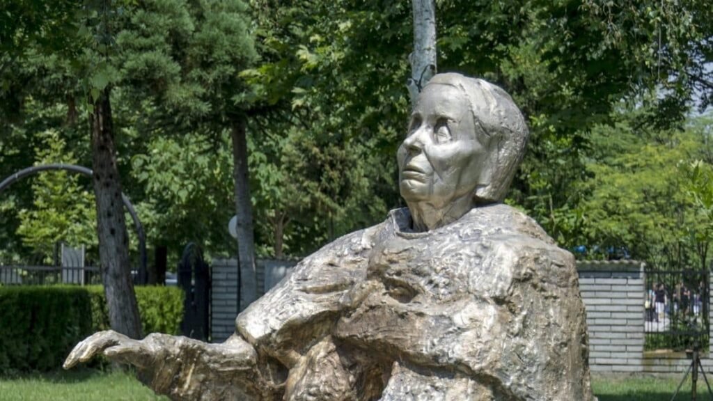 Бронзовая статуя Бабы Ванги в парке, вид сбоку с протянутой рукой