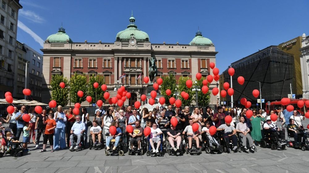 Участники акции крупным планом — дети в инвалидных колясках и их поддержка с красными воздушными шарами в центре Белграда
