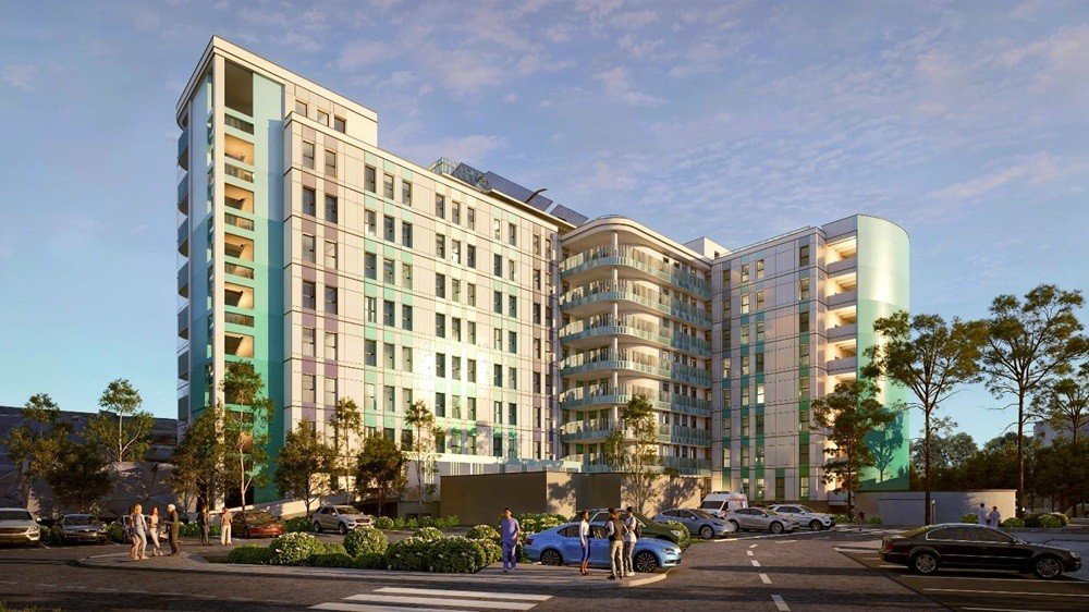 3D-визуализация нового комплекса «Мать и дитя» в Араде: вид на здание с улицы в вечернем освещении, парковка и зелёные насаждения у входа