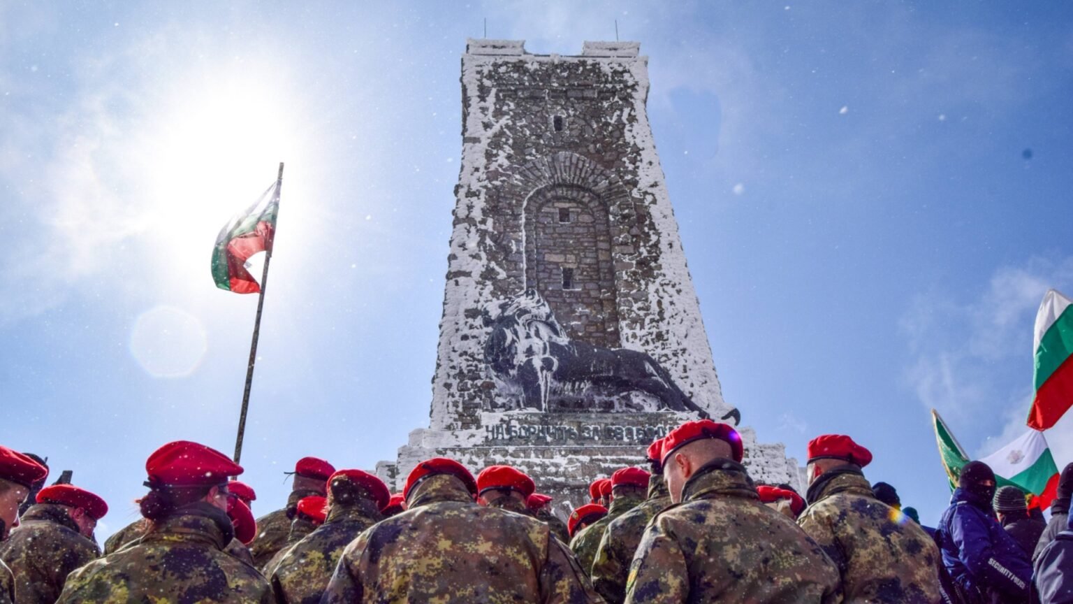 Памятник Свободы на Шипке с болгарскими солдатами в красных беретах и болгарским флагом на фоне голубого неба. Фото: Actualno.com