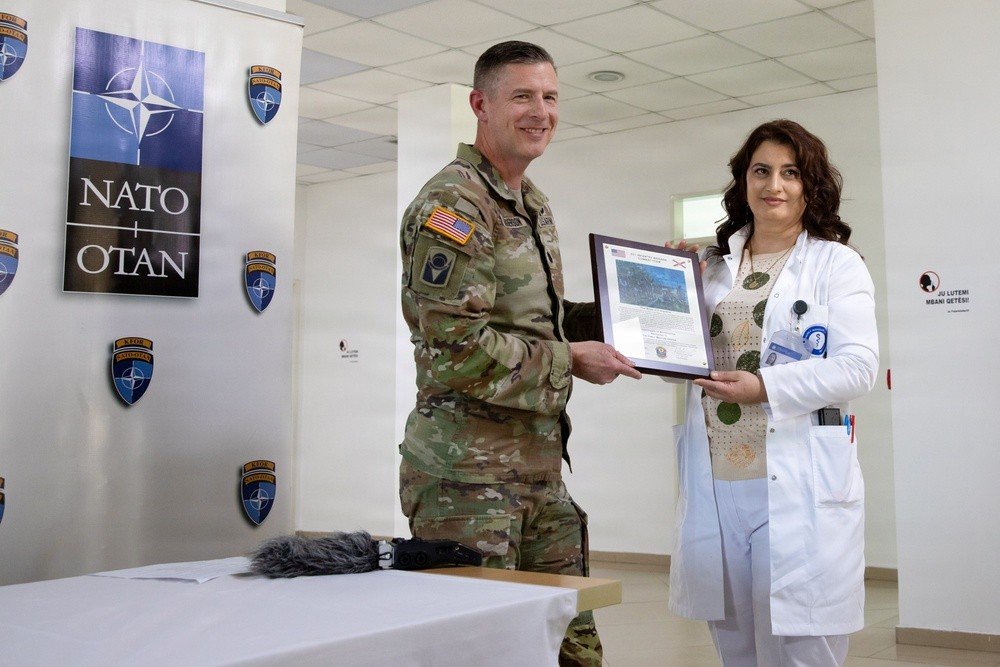 Офицер KFOR вручает благодарственный сертификат врачу Центра семейной медицины на церемонии передачи оборудования