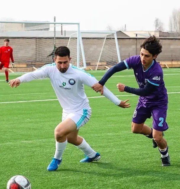 Два футболиста борются за мяч во время матча — игрок в белой форме и игрок ФК Ноа в фиолетовой форме