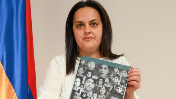 Эдита Гзоян держит фотографии жертв геноцида на фоне армянского флага