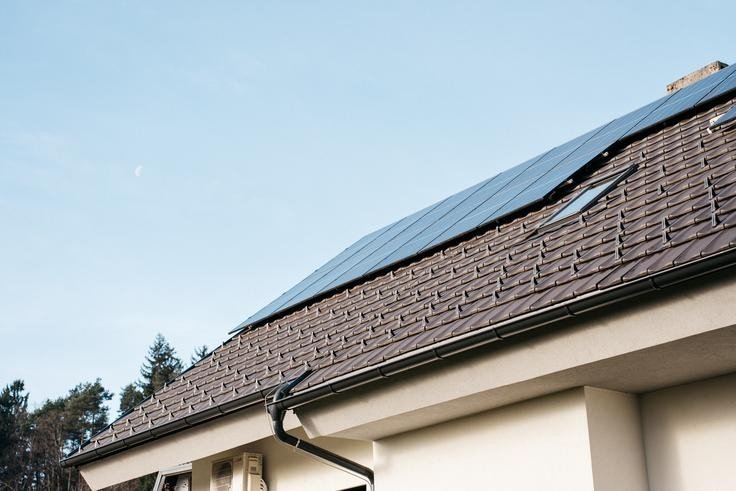 Солнечные панели на крыше частного дома с черепичной кровлей на фоне ясного неба