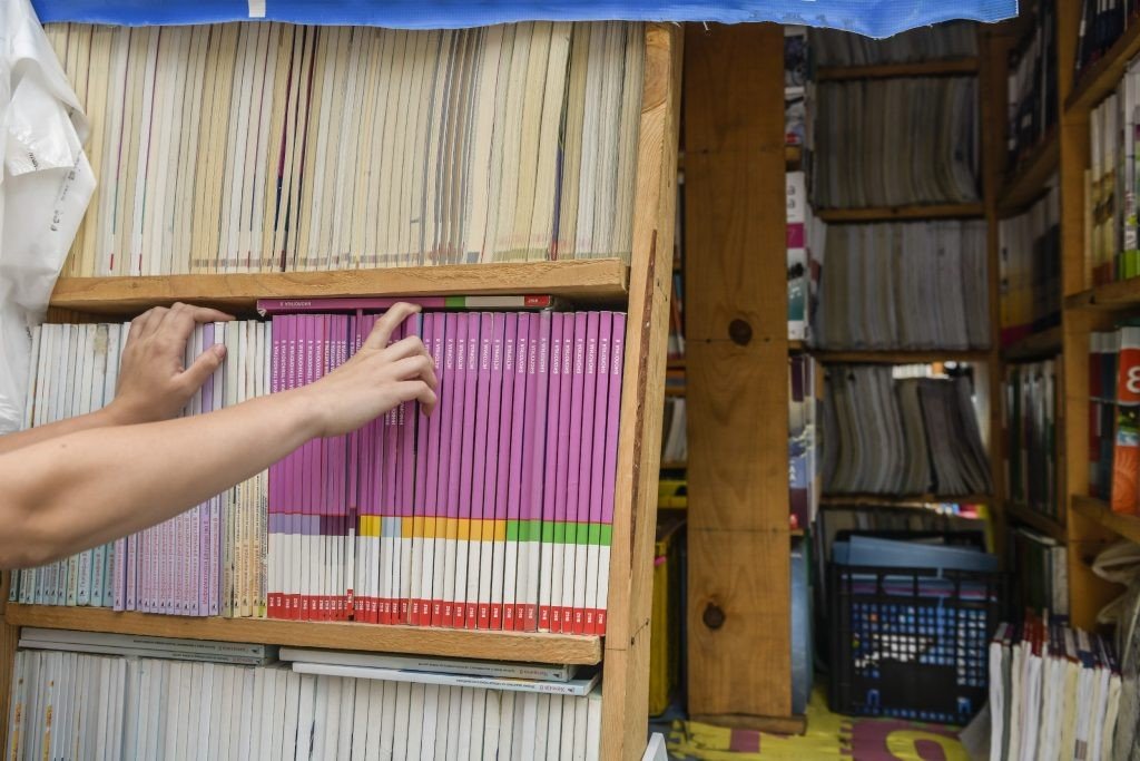 Рука достаёт учебник с полки книжного магазина