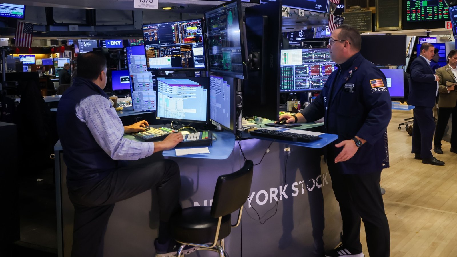 Трейдъри работят на търговския етаж на Нюйоркската фондова борса, заобиколени от множество монитори с финансови данни