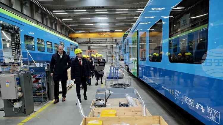 Делегация чиновников в касках осматривает сборочный цех завода Škoda, где на линии стоят голубые вагоны электропоездов для Болгарии