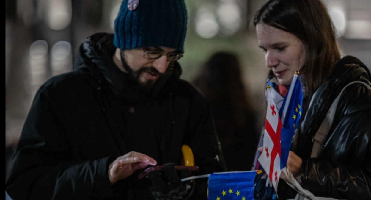 Двое протестующих что-то рассматривают вместе, держа в руках маленькие грузинский и флаг ЕС, символизируя проевропейскую ориентацию. Фото: Caucasian Knot