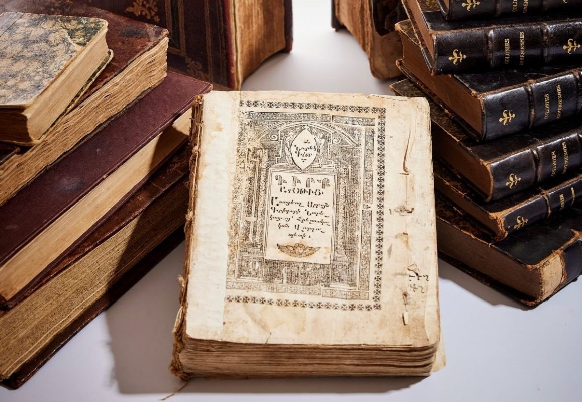 Старинная армянская книга с орнаментированным титульным листом, раскрытая среди кожаных томов из коллекции книжного магазина «Самуэлян»