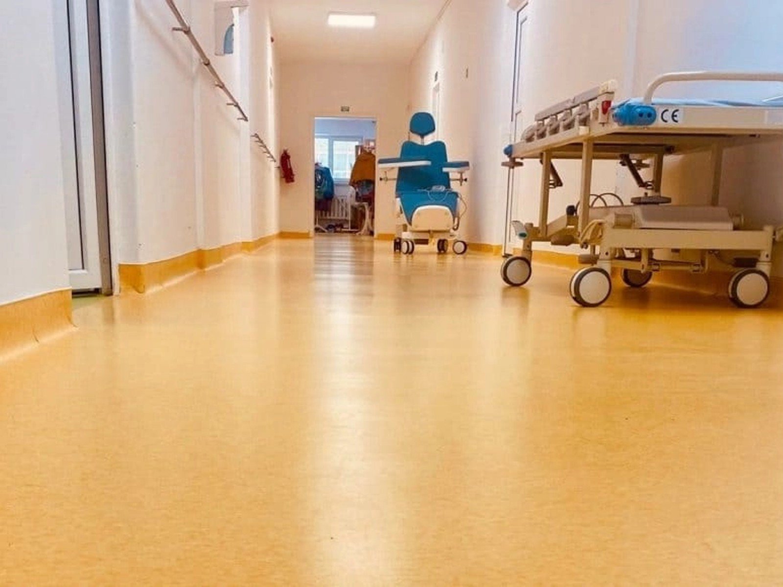 Пустой больничный коридор с жёлтым полом, инвалидным креслом и медицинской каталкой