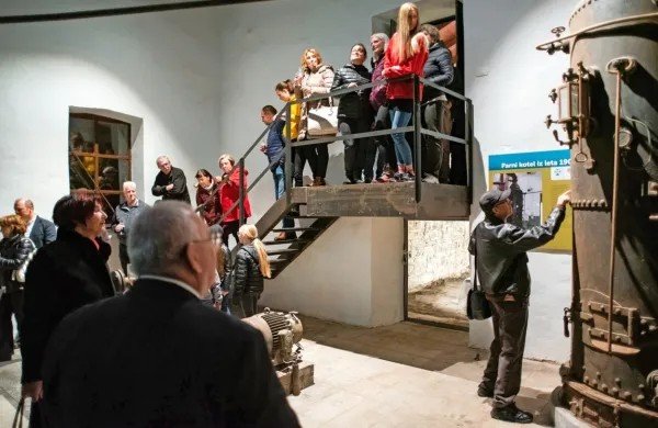 Посетители информационного центра осматривают экспозицию с историческим паровым котлом в сопровождении экскурсовода