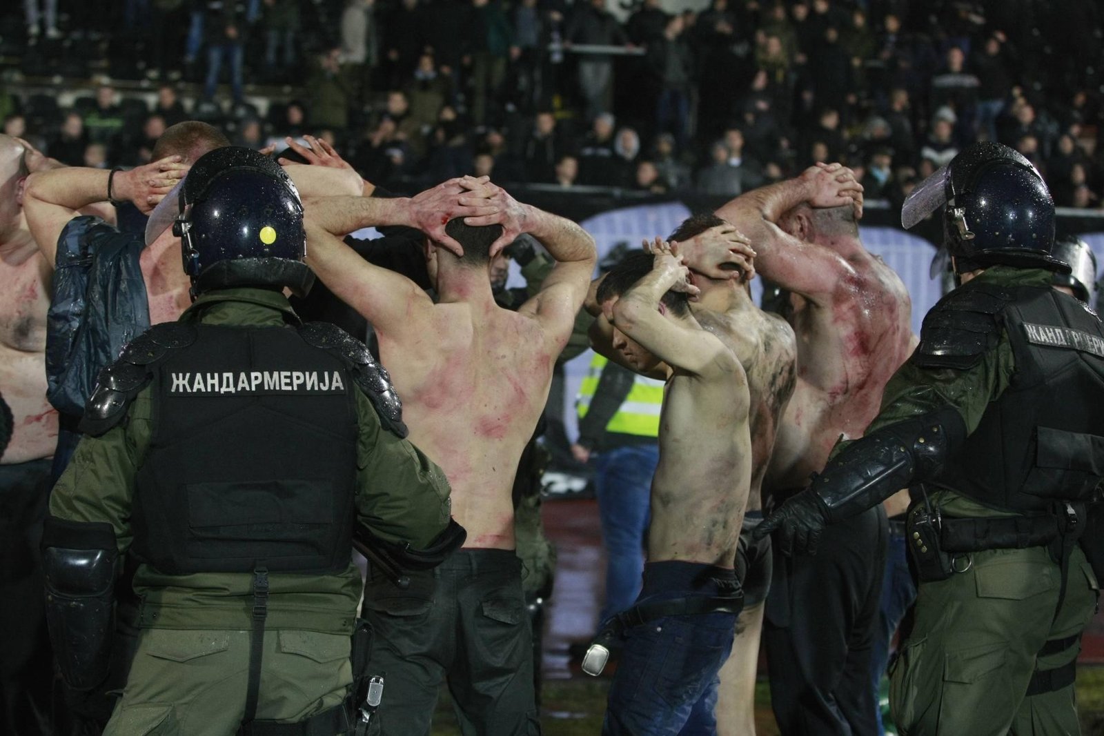 Бойцы сербской жандармерии задерживают людей с руками на голове на футбольном стадионе