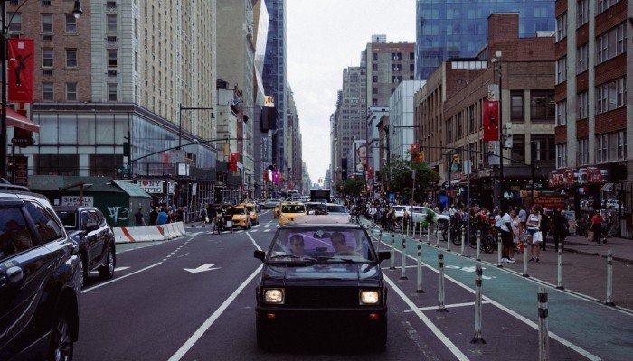 Yugo едет по широкой авеню в Нью-Йорке среди городского трафика — кадр из фильма «Yugo Goes to America»