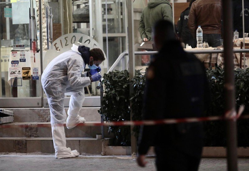 Криминалист в белом костюме собирает улики на месте стрельбы у здания в Греции