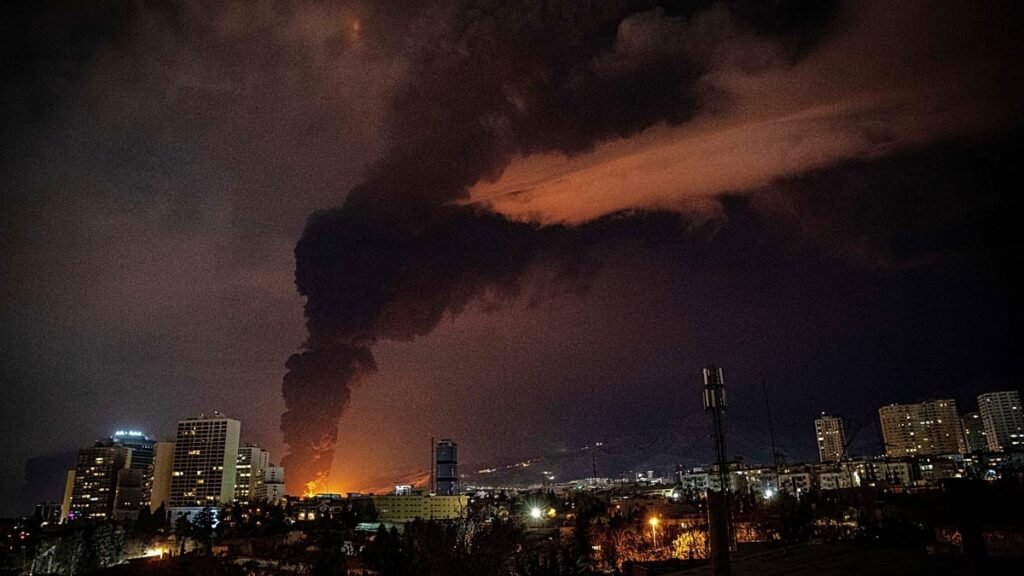 Румыния между Вашингтоном и Брюсселем: как война в Иране расколола ЕС Ночной вид на иранский город во время американских военных ударов — над городскими зданиями поднимается столб дыма и пламени, небо озарено огнём