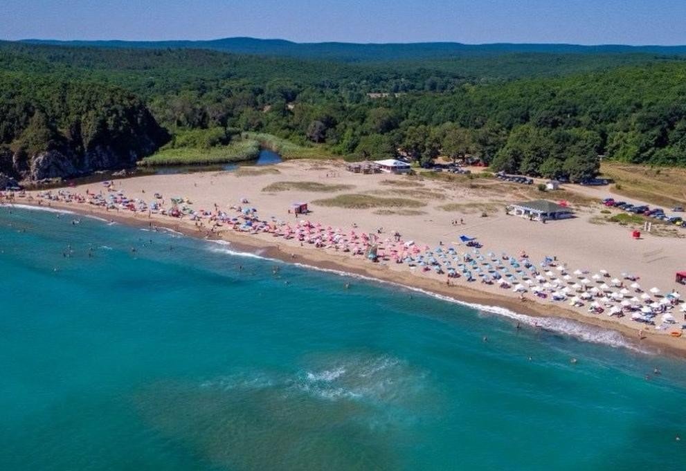 Вид с воздуха на болгарский пляж Бутамята с бирюзовой водой Чёрного моря, разноцветными зонтиками и зелёными холмами на заднем плане