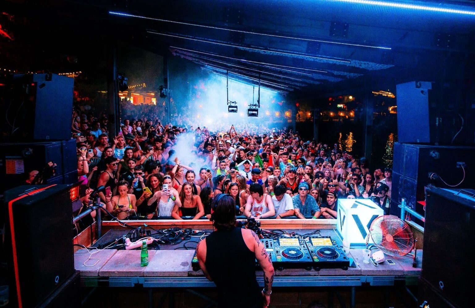 Диджей выступает за пультом перед переполненной танцевальной площадкой на фестивале Terminal V — синие прожекторы и сценический дым создают электрическую атмосферу