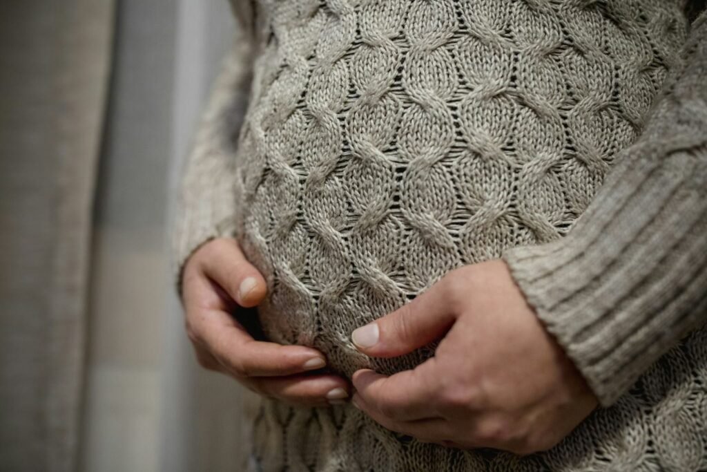 Крупный план беременной женщины в вязаном свитере, бережно обнимающей живот