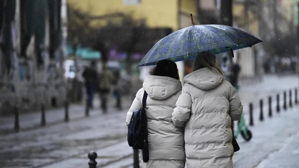 Болгарию ждёт холодная неделя: дожди, снег и до +14° Двое прохожих в зимних куртках идут под зонтом по дождливой городской улице