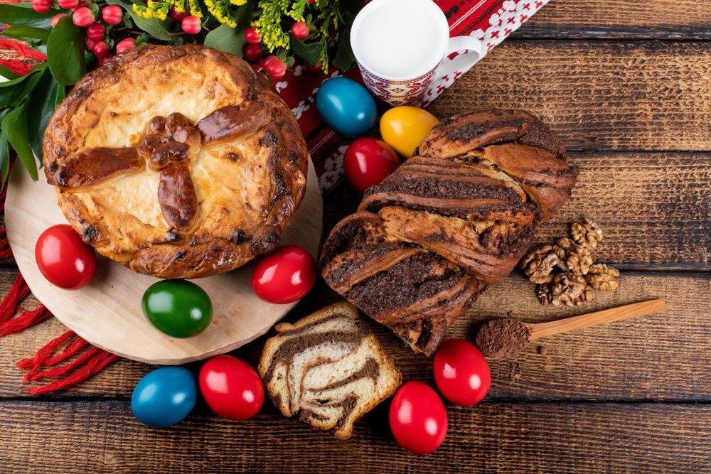 Традиционный румынский пасхальный стол с паской, нарезанным козонаком с грецкими орехами и разноцветными крашеными яйцами на деревянной поверхности