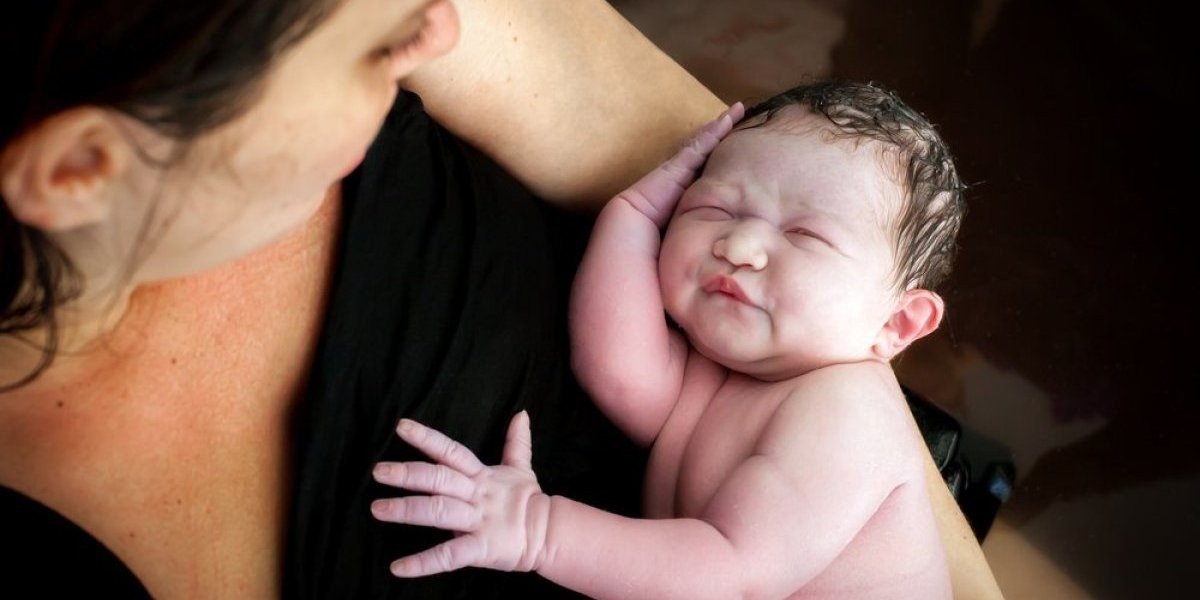 Мать держит новорождённого ребёнка на руках после родов