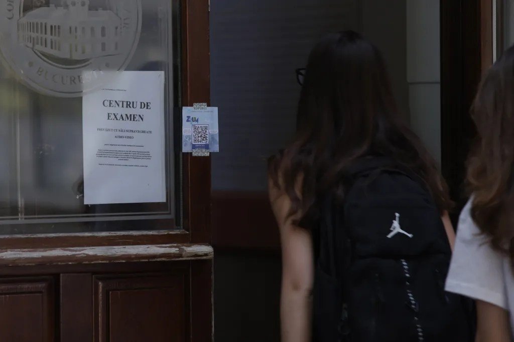 Выпускницы входят в экзаменационный центр в Бухаресте — на двери объявление «Centru de examen»
