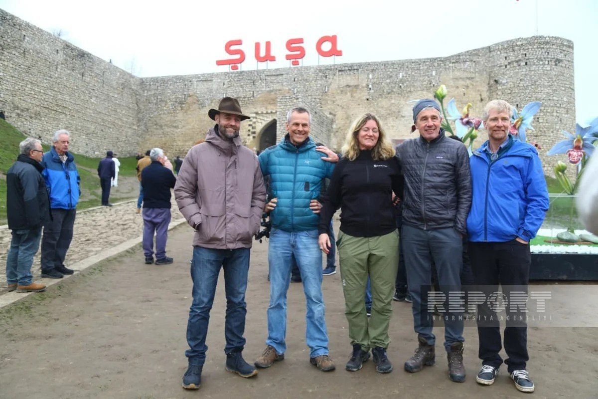 Группа международных путешественников позирует на фоне крепостных стен Шуши и надписи «Şuşa»