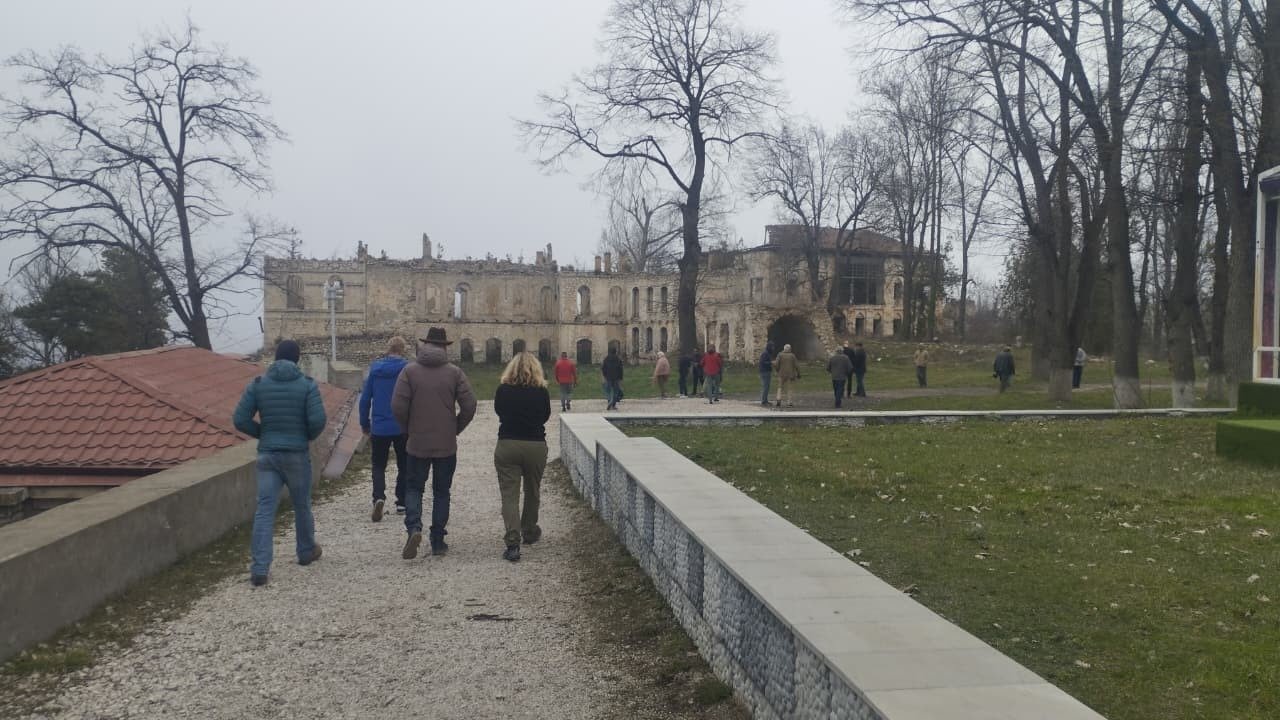 Участники поездки идут по дорожке к историческому зданию в Шуше, пострадавшему во время конфликта