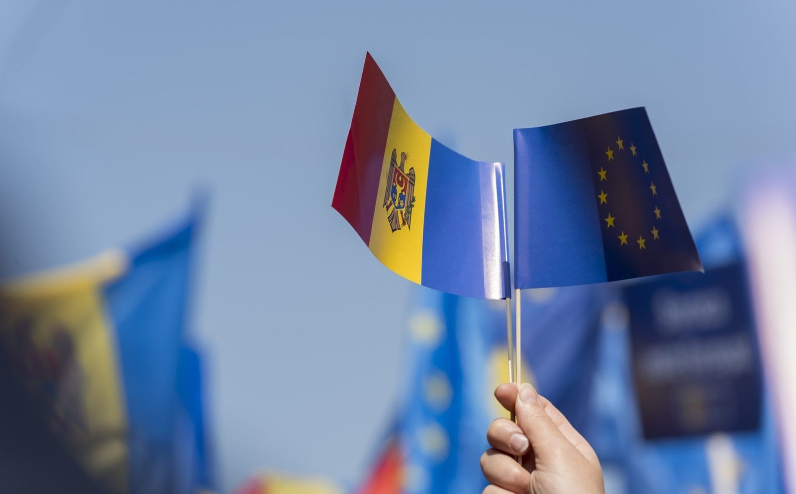 Флажки Молдовы и Евросоюза в руке на фоне голубого неба — символ европейских устремлений страны
