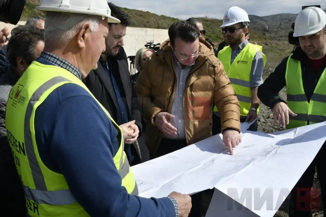 Чиновники и инженеры в защитных касках изучают проектные чертежи плотины на строительной площадке