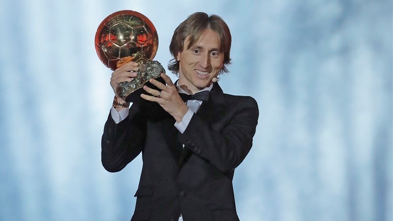 Лука Модрич держит «Золотой мяч» на церемонии вручения награды в Париже в 2018 году, одетый в чёрный смокинг