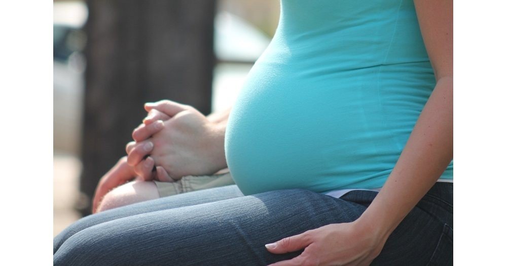 Беременная женщина сидит, сложив руки на коленях, крупный план живота