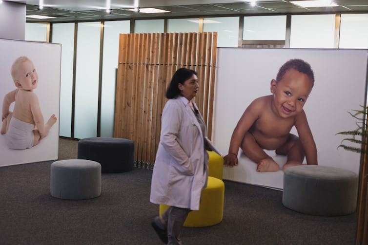 Холл клиники репродуктивной медицины в Грузии с большими фотографиями младенцев на стенах и проходящей мимо сотрудницей в белом халате