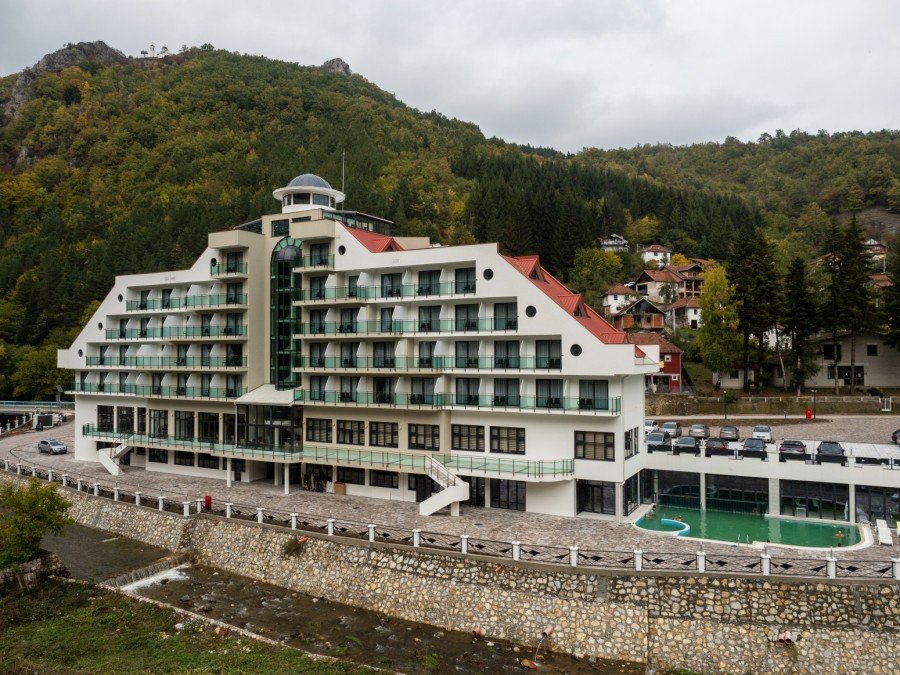 Многоэтажный спа-отель с бассейном у подножия покрытых лесом гор в осеннем убранстве