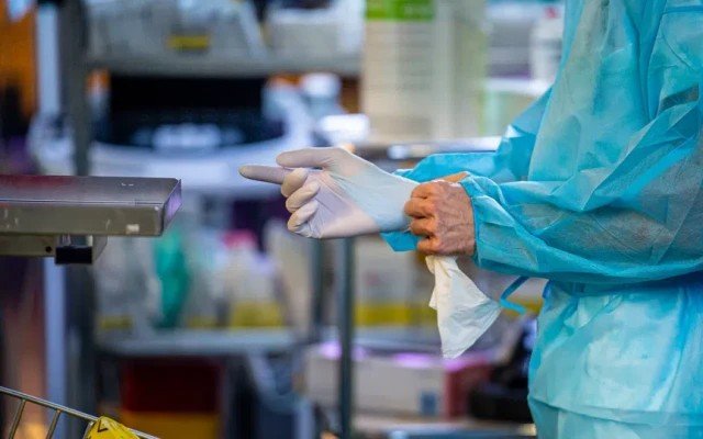 Медицинский работник в хирургическом халате надевает защитные перчатки