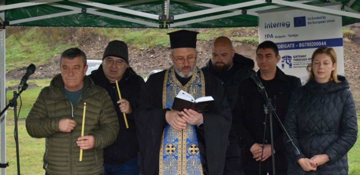 Священник совершает водосвятный молебен на церемонии начала реставрации крепости Русокастро, на заднем плане — баннеры программы Interreg