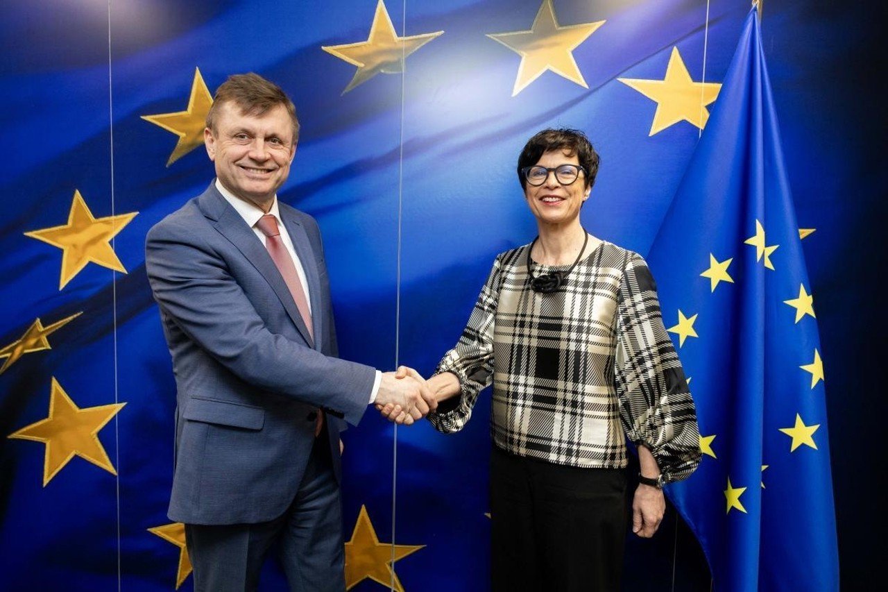 Молдавский чиновник пожимает руку представителю ЕС на фоне флагов Евросоюза