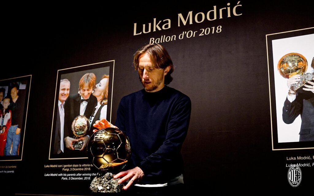 Лука Модрич устанавливает свой «Золотой мяч» 2018 года на стенд выставки в музее Mondo Milan, на заднем плане видны фотографии из его карьеры