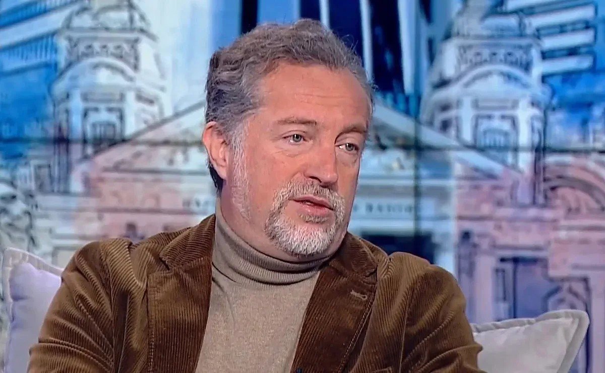 Ivo Hristov during a TV interview wearing a brown corduroy jacket, studio background with parliament imagery. Фото: Standart News