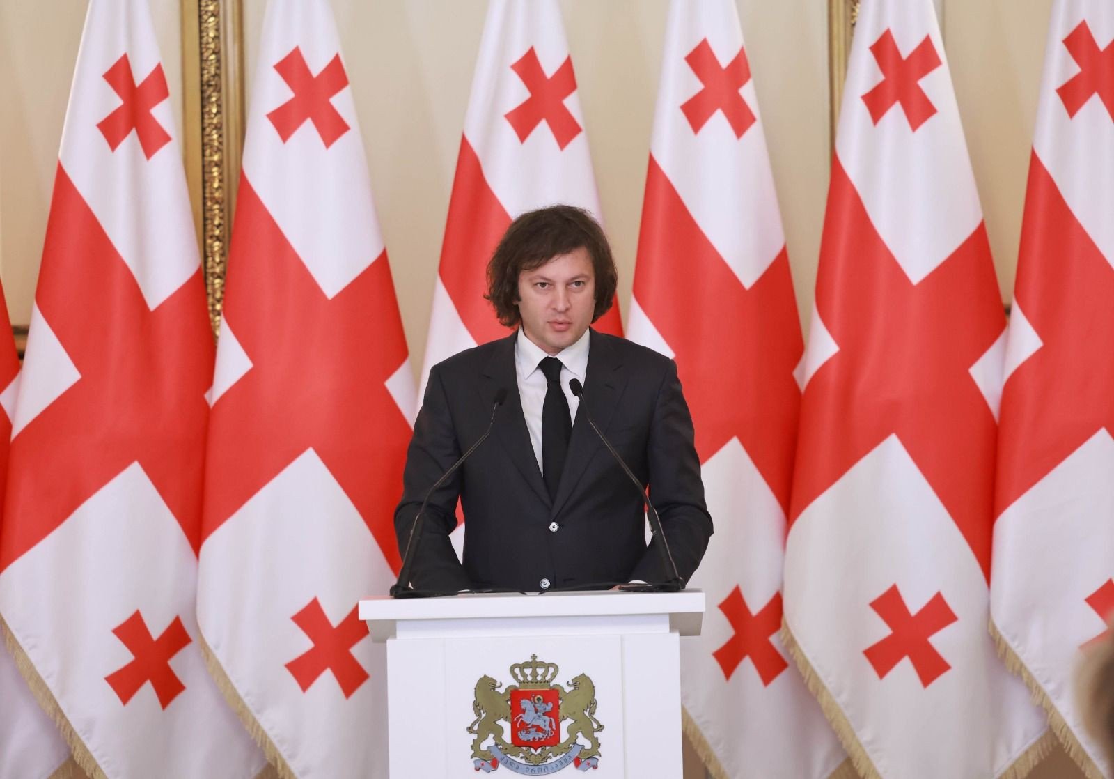 Премьер-министр Грузии Ираклий Кобахидзе выступает на трибуне на фоне грузинских флагов. Фото: Civil Georgia